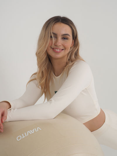 Blonde model is wearing a long sleeve crop top and leggings in eggnog cream.  The WKND logo is green and printed centrally to the chest.  The models is posing with a yoga ball.