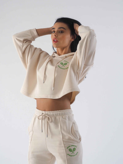 Model with dark hair, running hand through hair. Model is wearing an eggnog tracksuit with green embroidery