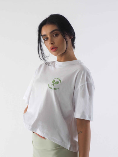 Model with dark hair wearing an oversized cropped white t-shirt. The WKND Apparel tennis logo is embroidered to the chest.