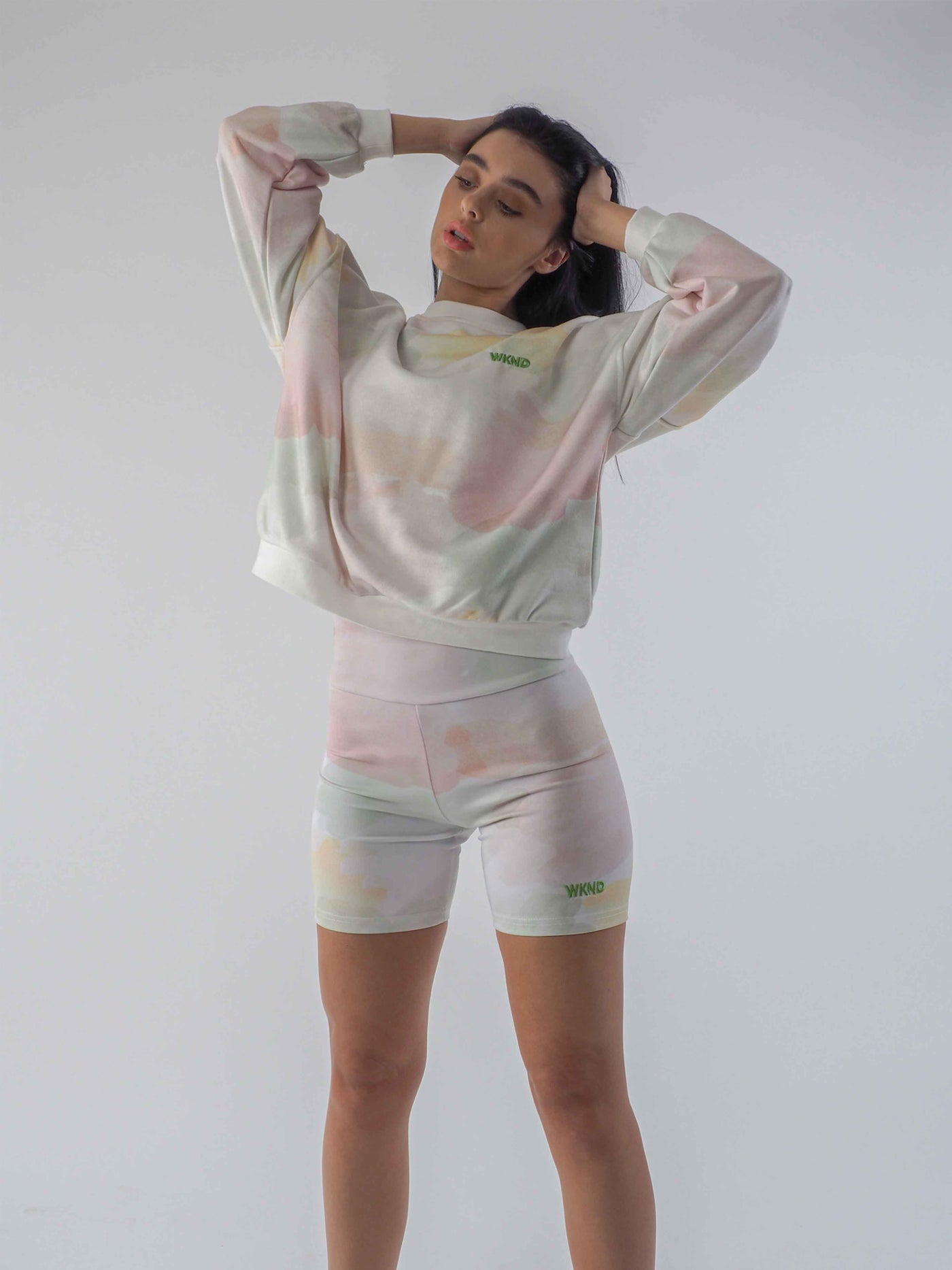 Model has dark hair and is wearing watercolour tie die sweatshirt with matching cycling shorts.