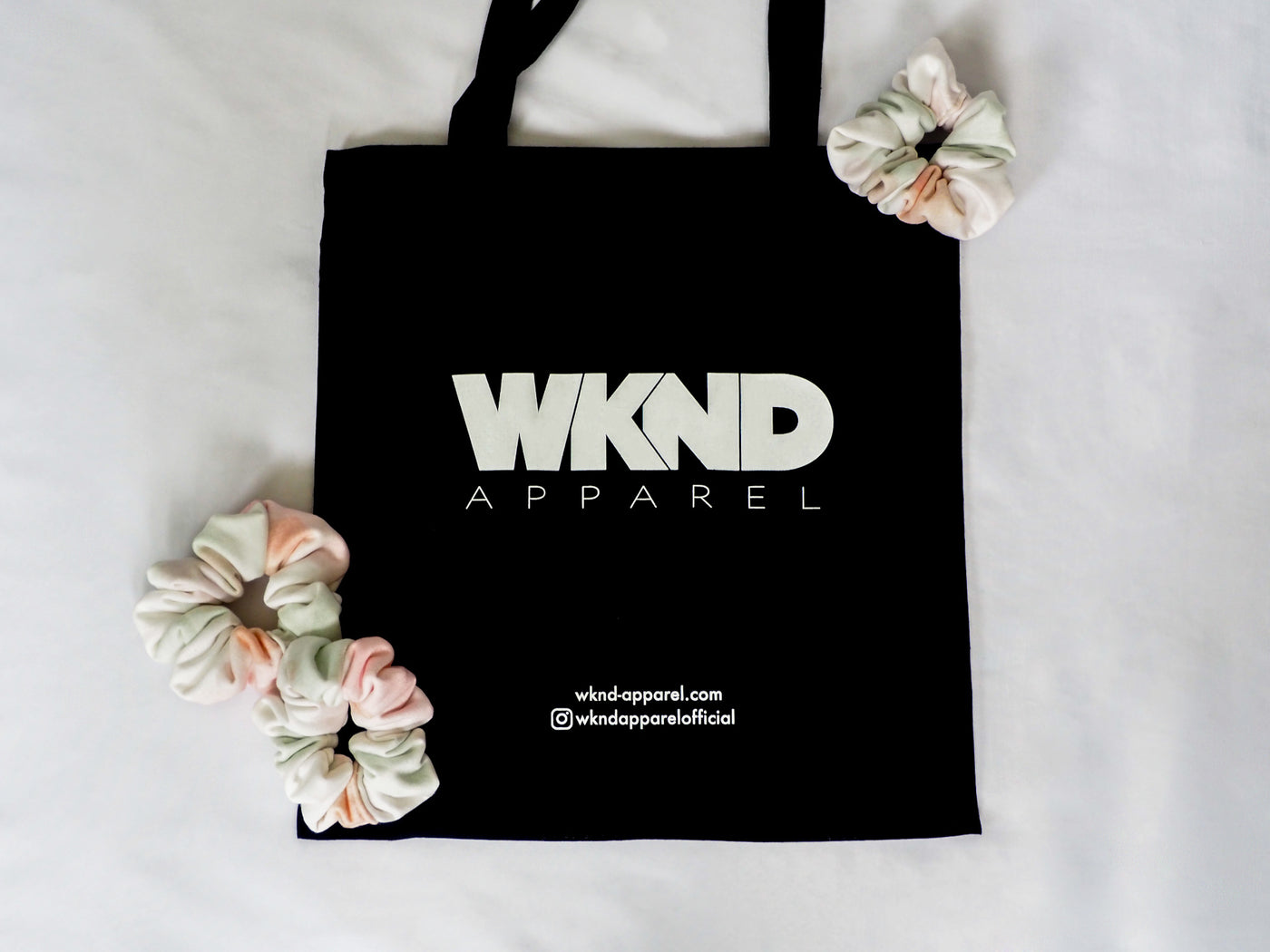 handmade scrunchies in watercolour tiedye print displayed with black cotton tote bag with wknd apparel branding