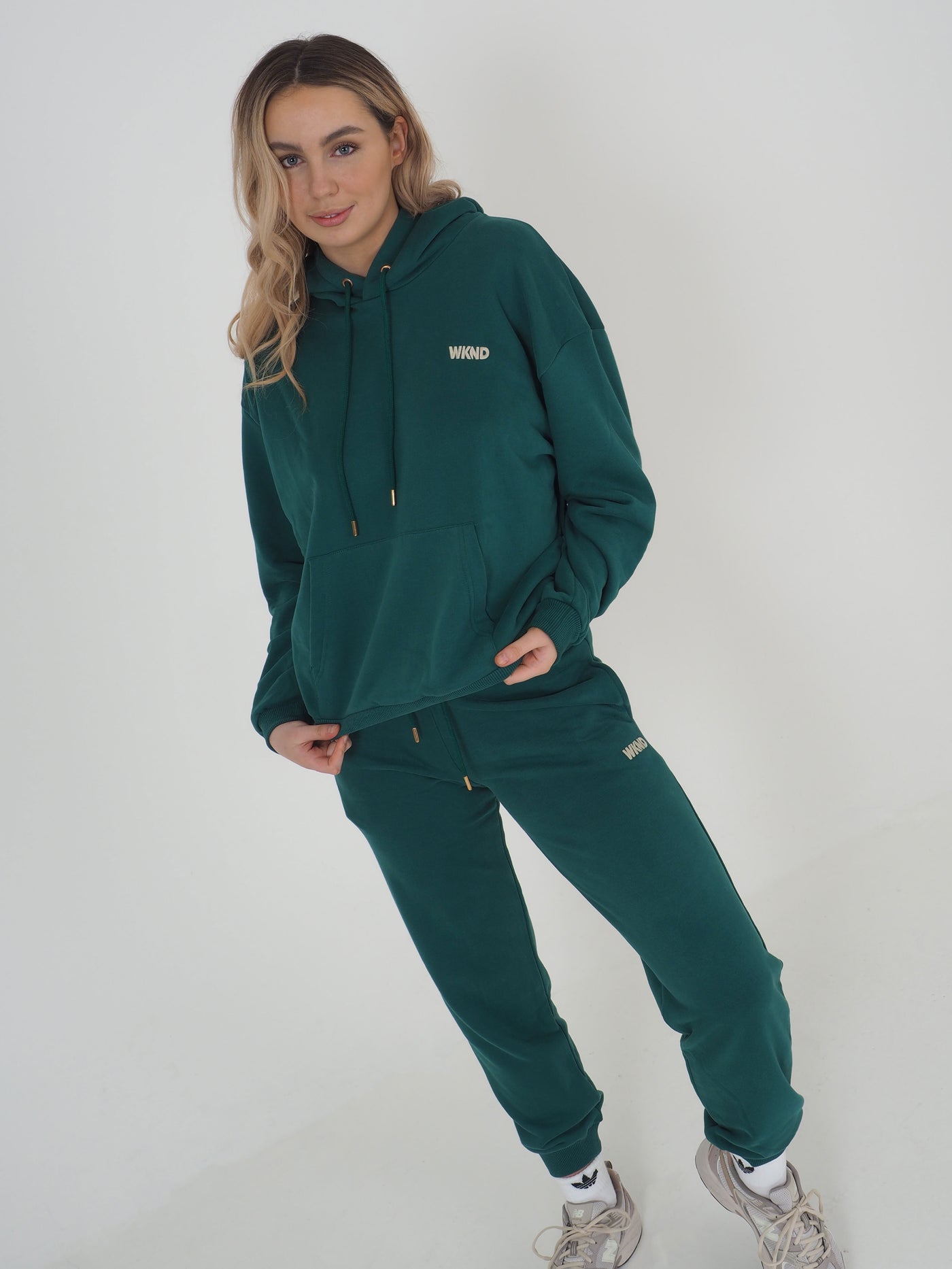 Model with blonde hair is wearing a green hoodie and matching joggers. WKND Embroidery to the chest and leg.