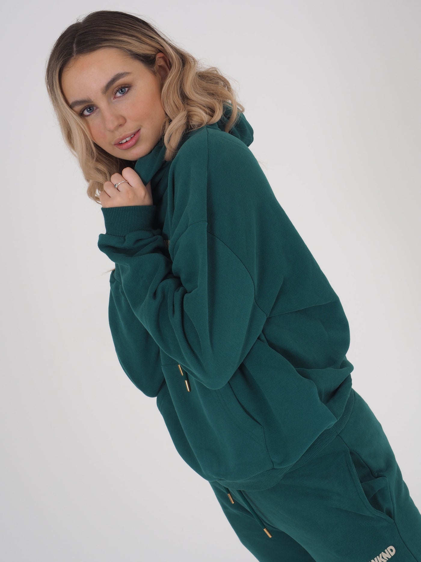 Model with blonde hair is wearing a green hoodie and matching green joggers.