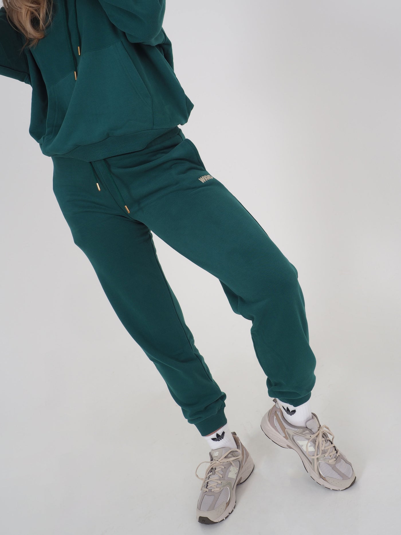 Model wearing green joggers and matching hoodie. WKND is embroidered to the leg.