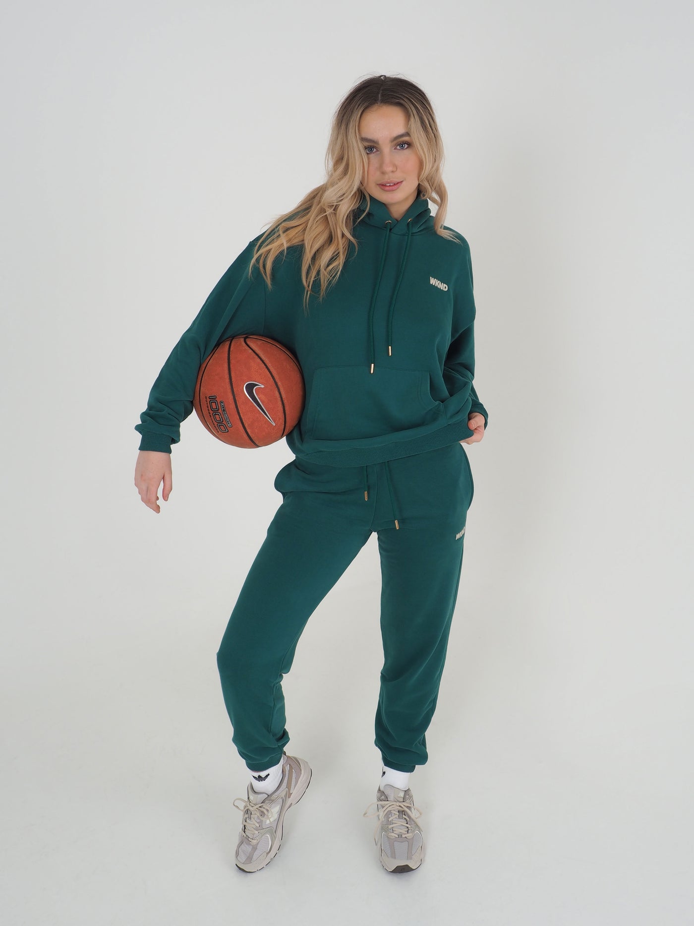 Model is blonde, holding a basketball and wearing matching green hoodie and joggers.