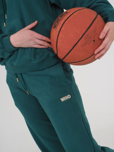 Close up of model wearing WKND joggers.  The WKND logo is embroidered to the leg and the model is holding a basketball.