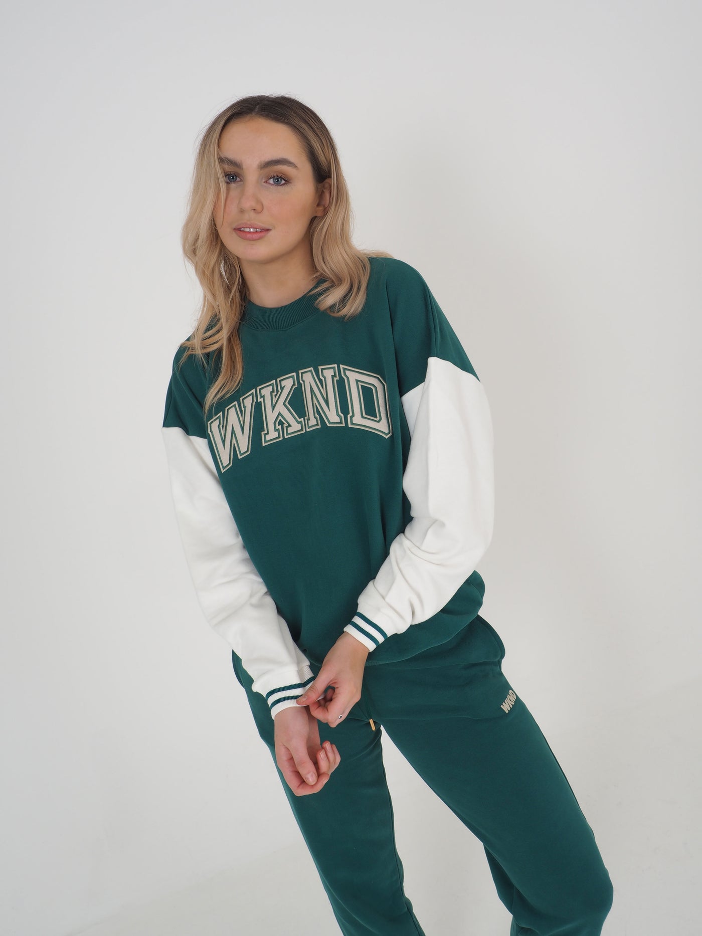 Model with blonde hair wearing a green college varsity style sweatshirt and matching joggers.  Sweatshirt has contrast white sleeves and the text reads WKND.