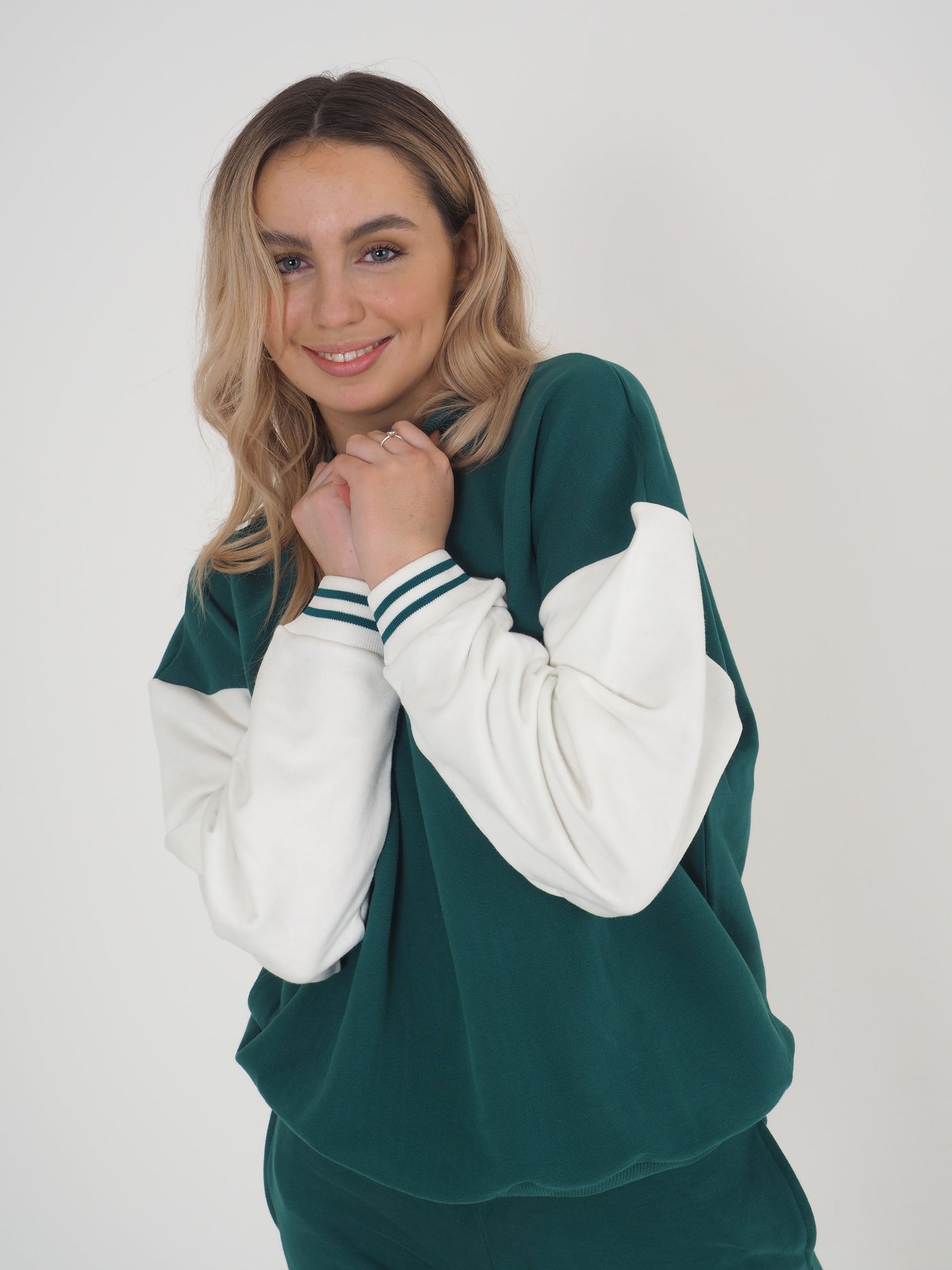 Model with blonde hair wearing a green college varsity style sweatshirt and matching joggers.  Sweatshirt has contrast white sleeves.