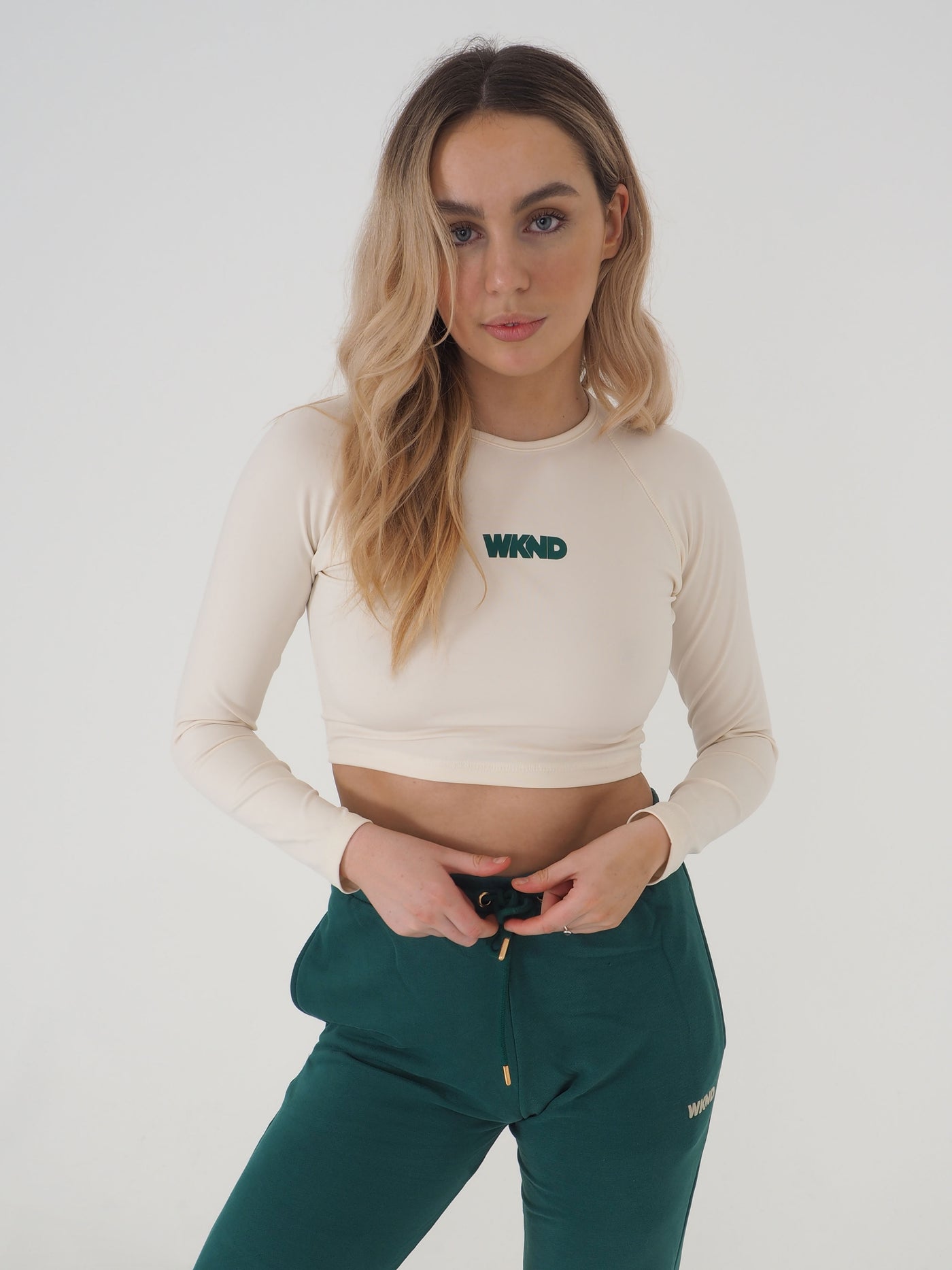 Blonde model is wearing a long sleeve crop top in eggnog cream and matching green joggers.  The WKND logo is green and printed centrally to the chest.