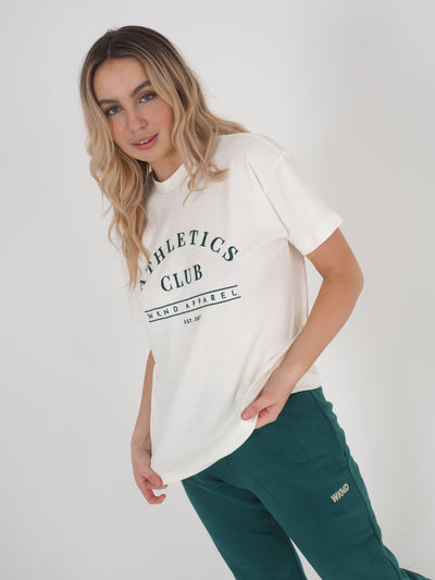 Blonde model wearing a white oversized t-shirt and matching green joggers.  T-shirt embroidery spells Athletics Club, WKND Apparel, established 2021.