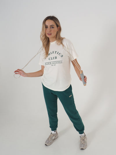 Blonde model is posing with a skipping rope and is wearing a white oversized t-shirt and matching green joggers.  T-shirt embroidery spells Athletics Club, WKND Apparel, established 2021.