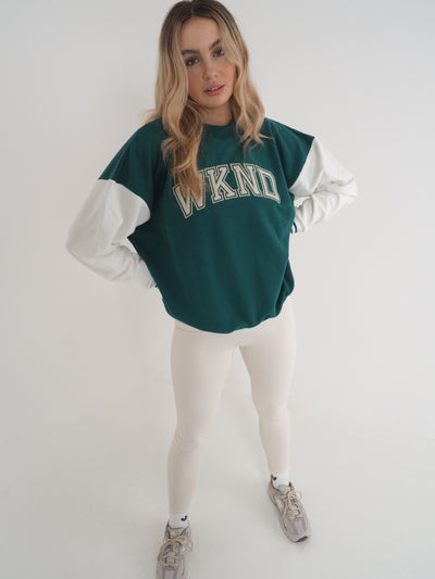 Model with blonde hair wearing a green college varsity style sweatshirt with eggnog leggings.  Sweatshirt has contrast white sleeves and the text reads WKND.