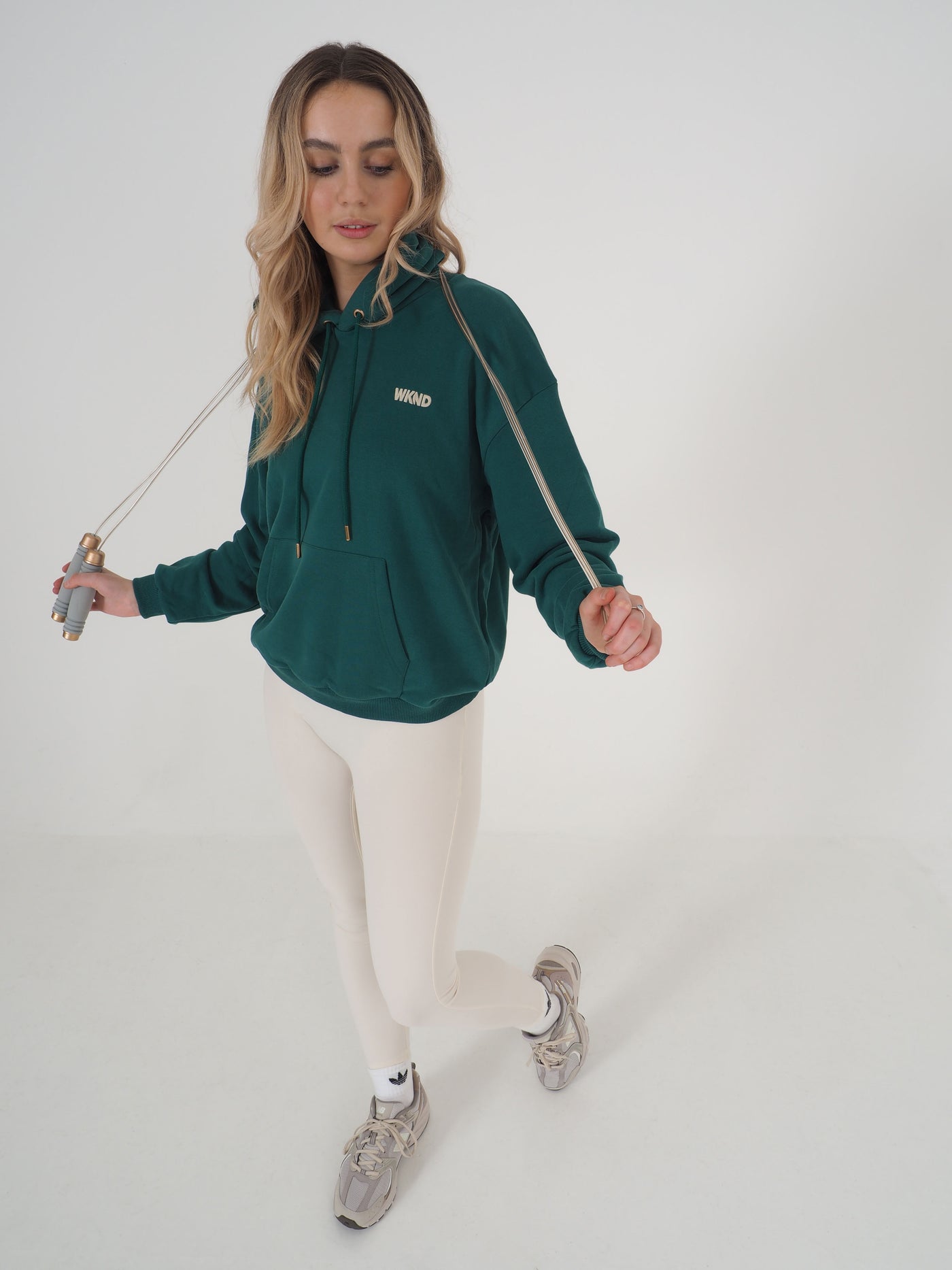 Blonde model is posing with skipping rope and wearing green hoodie and eggnog leggings.